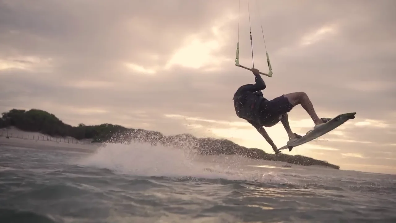 Kitesurfista manobrando sobre a água ao entardecer